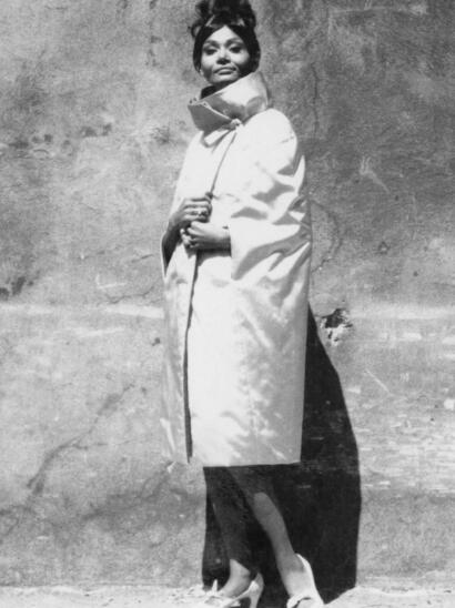 Black-and-white photo of a woman in elegant fashion, wearing a long coat, high heels, and a scarf.